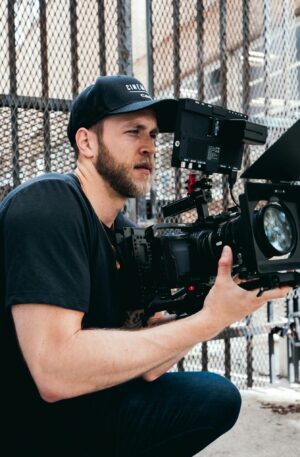 A male cinematographer operates a high-end camera outdoors, capturing footage.