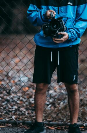 A man holding a camera stands by a wire fence, showcasing casual outdoor photography setup.