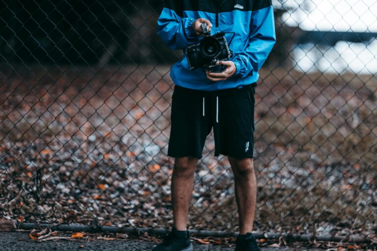 A man holding a camera stands by a wire fence, showcasing casual outdoor photography setup.