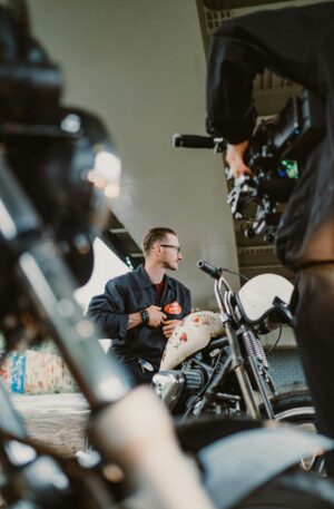 A motorcyclist poses under a bridge while being filmed, showcasing urban culture.
