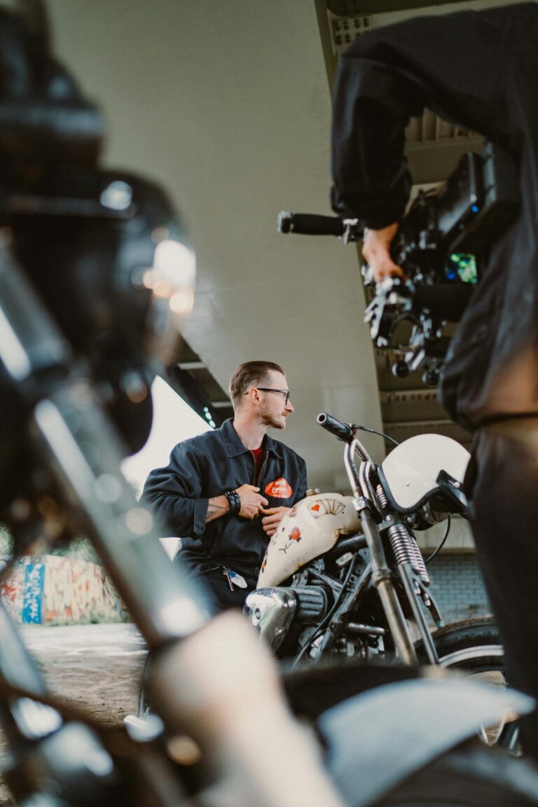 A motorcyclist poses under a bridge while being filmed, showcasing urban culture.