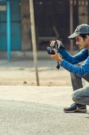 A young man crouching to take photos with his DSLR camera in an urban environment.